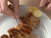Skewer being inserted in grilled meat on plate for preparation of schnitzel, step 3