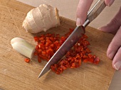 Chilli being finely chopped with knife on cutting board for preparation of pork, step 2