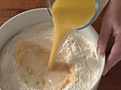 Liquid being added to flour in bowl for preparation of sesame bagel, step 1