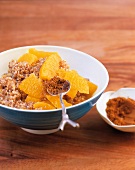 Grits and pieces of oranges in bowl and cinnamon powder on spoon over bowl