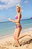 Portrait of pretty blonde woman wearing sports bikini running on beach, smiling