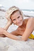 Pretty blonde woman wearing tube top bikini lying on beach with head on hand, smiling