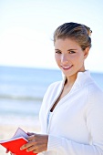 Dunkelblonde Frau, in Weiß gekleidet, steht am Strand