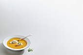 Carrot soup with smoked fish mousse and parsley in bowl on white background