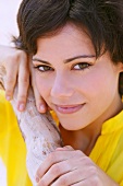 Close-up of beautiful brown eyed brunette woman leaning against branch, smiling