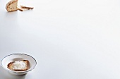 Parmesan grated on slice of bread in bowl and bread slices on white background, copy space