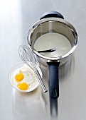 Sauce pan with milk and bowl with egg yolks and beater on it