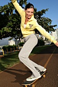 Schwarzhaarige Frau im gelben Pulli auf einem Skateboard
