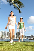 Two women jumping rope in a park under palm trees by the sea