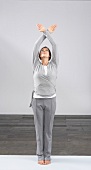 Woman in grey sportswear standing and exercising with hands crossed above head, looking up