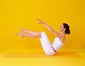 Pilates - Boomerang: Frau sitzt, Beine gebeugt heben, Arme vorne