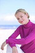 Portrait of pretty blonde woman wearing pink turtleneck sweater on the beach, smiling