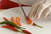 Chilli pepper being cut lengthwise with knife, step 1