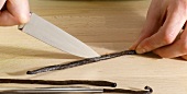 Vanilla beans being cut lengthwise with knife, step 1
