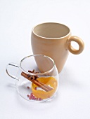 Clay cup and punch glass with orange peel and cinnamon on white background