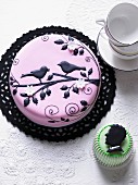 A cake decorated with pink fondant and black birds on a branch