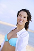 Portrait of pretty brunette woman wearing white blouse over blue bikini, smiling widely