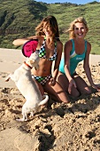 Zwei Frauen spielen mit einem Hund am Strand