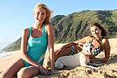Zwei Frauen sitzen mit Hund am Strand