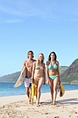 Mann und zwei Frauen gehen am Strand mit Surfbrett