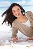 Portrait of happy woman wearing beige sweater lying on a blanket on sand, laughing