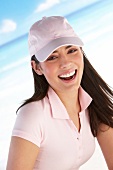 Portrait of pretty woman wearing pink polo shirt and cap standing on beach, laughing