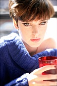 Portrait of green eyed woman with short hair in blue sweater holding red glass with drink