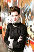Portrait of pretty woman wearing black fur jacket standing with arms crossed against wall