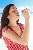 Frau am Strand trinkt aus einer Wasserflasche