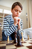 Pensive boy wearing striped sweater sitting and playing chess