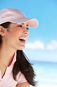 Side view of happy brown haired woman wearing pink cap and polo t-shirt, laughing