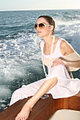 Frau mit Sonnenbrille auf Boot, Fuß baumelt im Wasser