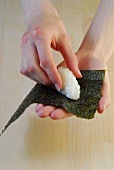 Shaped rice being placed on nori sheet for preparation of sushi, step 1