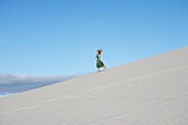 Pretty blonde woman wearing green dress running on sand dune in desert
