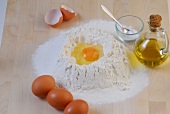 Egg yolk in flour with oil jar beside while preparing noodles, step 1