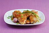 Braised chicken with shallots and garlic garnished with chives on plate