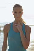 Portrait of woman exercising by touching her thumb and middle finger to clavicle on beach