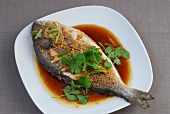 Fried bream fish with spicy sauce garnished with coriander leaves on plate