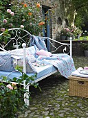 Rose-patterned cushions and blankets in shades of blue on metal-framed day bed in garden