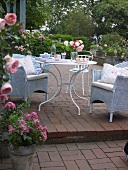 Table and wicker chairs with roses around in garden