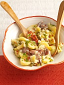 Silesian potato salad with pickled herring, bacon and cucumber in bowl