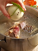 Onion, cloves and bay leaves being added to water while preparing beef broth, step 2