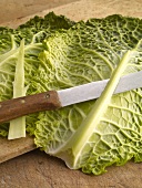 Close-up of cabbage ribs being cut with knife while preparing savoy roulades, step 1