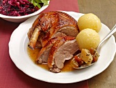 Stuffed goose with red cabbage, potato dumplings and gravy on plate