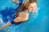 Vogelperspektive: Frau, blaues Hemd, geschminkt, schwimmt im Pool