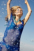Happy woman wearing blue transparent top on bikini laughing and splashing water drops