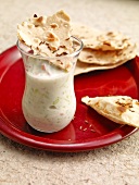 Glass of gurkenraita with toasted pita bread and caraway on red plate