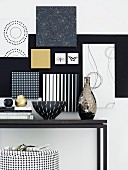 Frames covered in various black and white wallpapers on wall above black console table