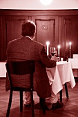 Man sitting on table with lit candle, holding red glass wine