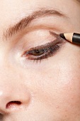 Close-up of woman applying eye liner, looking down